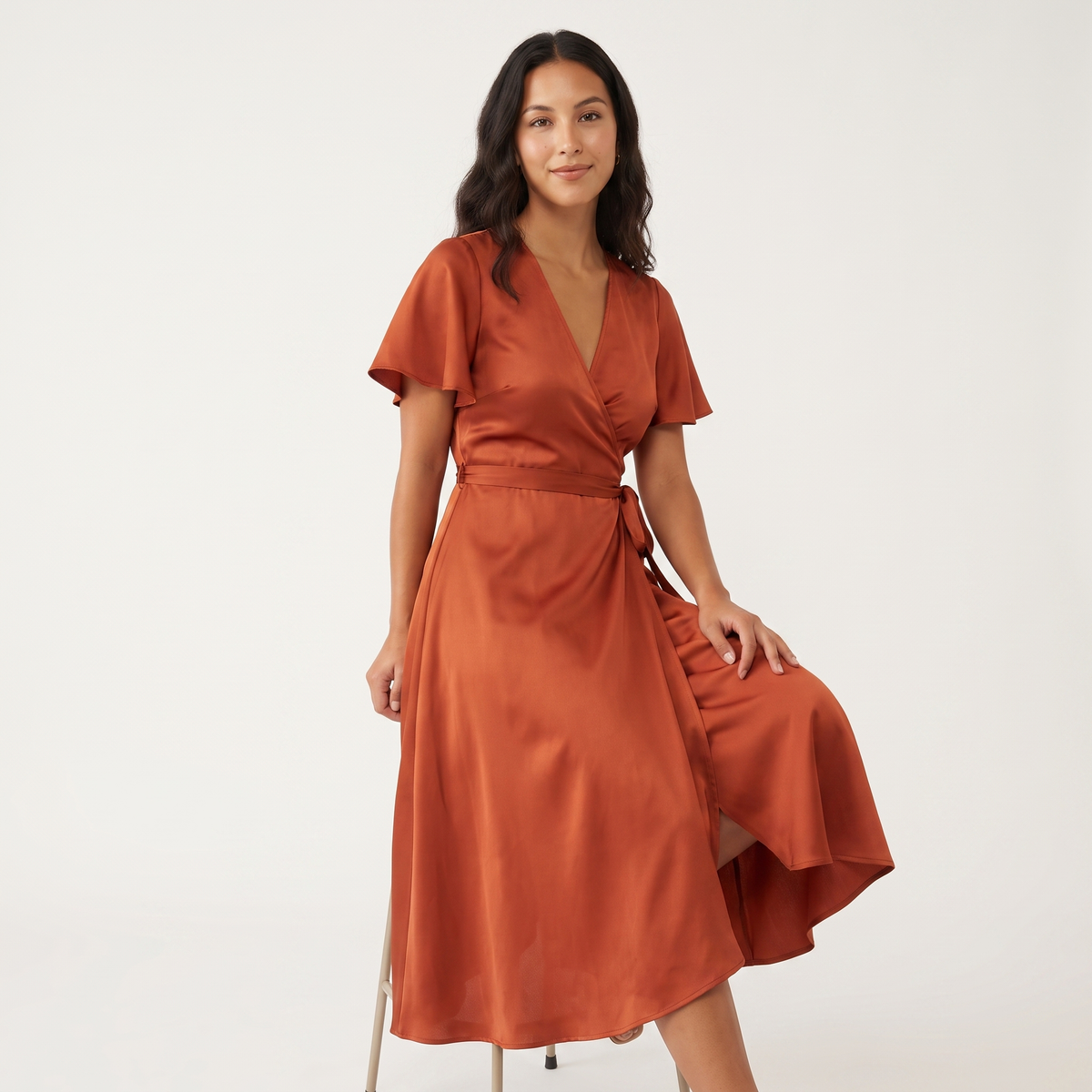 Model seated wearing rust satin wrap midi dress