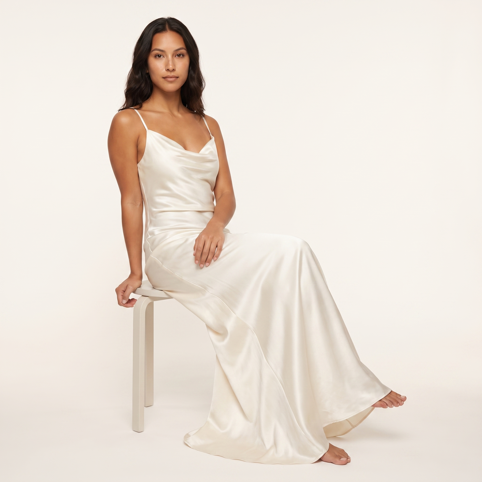 Model seated wearing ivory satin slip maxi dress