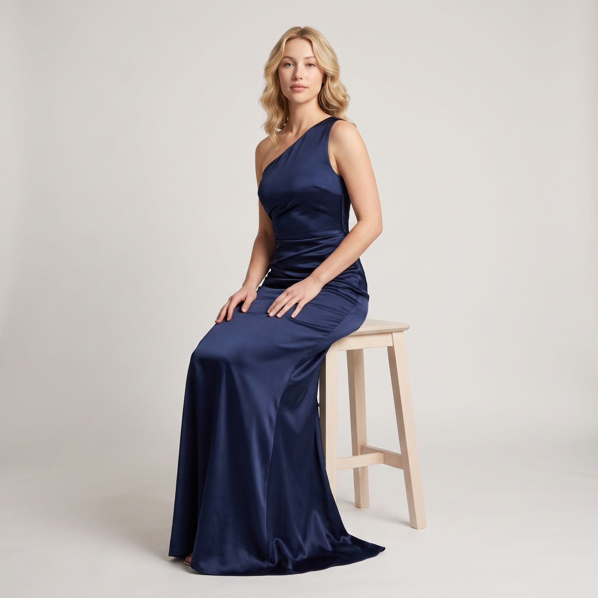 Model seated wearing navy one-shoulder satin gown