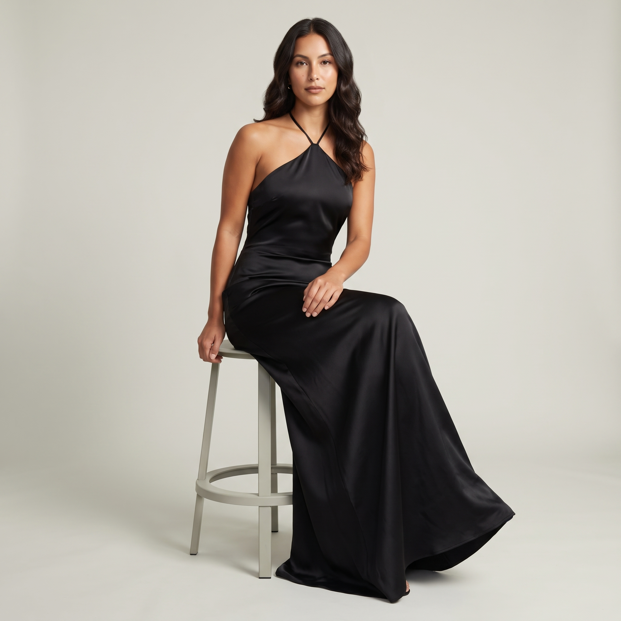 Model seated wearing black satin halter maxi gown